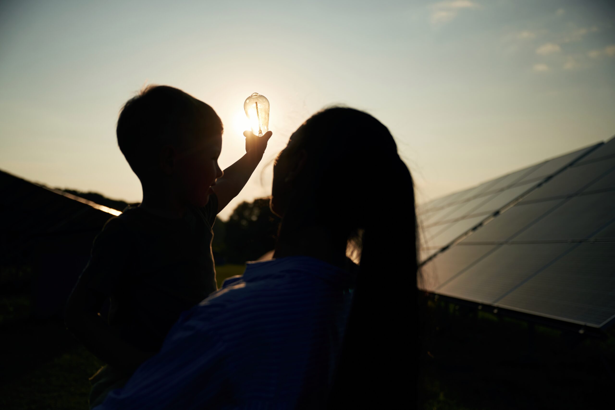 Darkened, against the sun, with light bulb, hope. Mother with her little son are near the solar panels